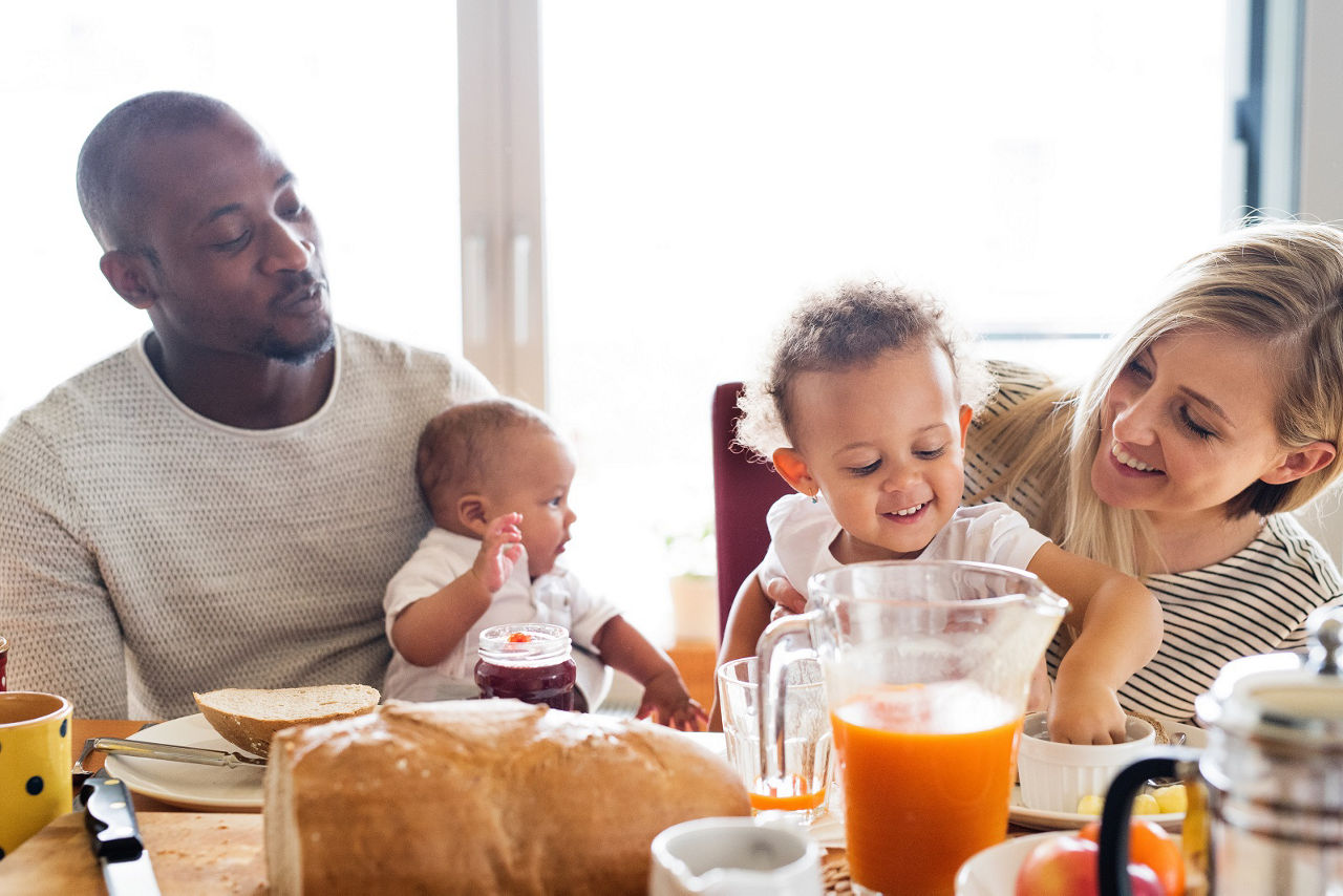 Young interracial family with little children having breakfast.