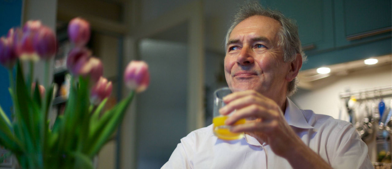Man drinking orange juice in kitchen with a bouquet of tulips in the foreground