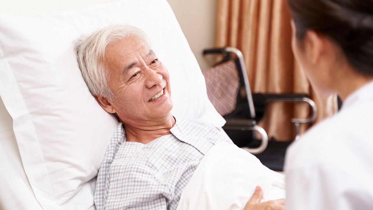 young asian doctor talking to senior patient at bedside in hosptial ward