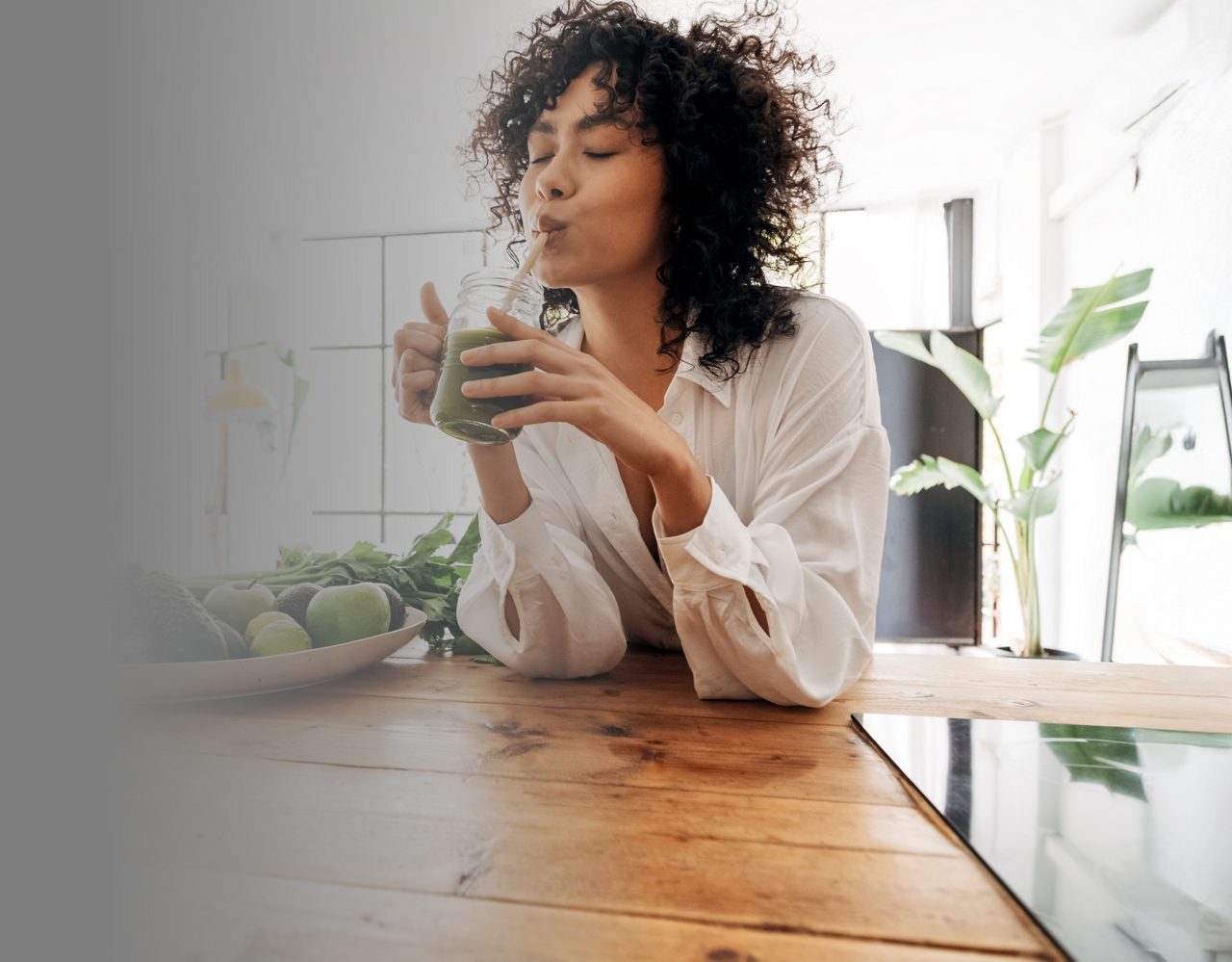 African American woman smiling while drinking a glass of green juice, enjoying a healthy lifestyle.
