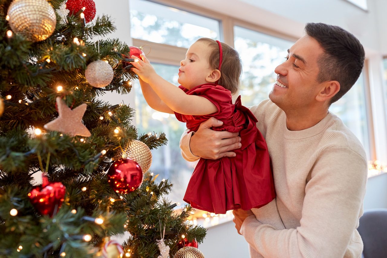 Vader draagt ​​zijn kind terwijl hij naast een versierde kerstboom staat en een vreugdevol vakantiemoment deelt.