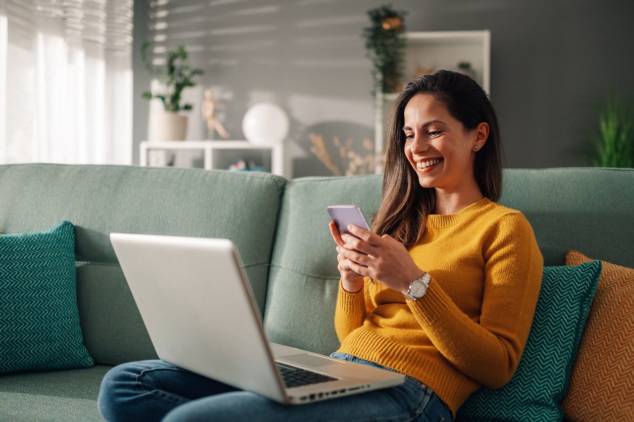 Vrouw multitasking met een laptop en smartphone.