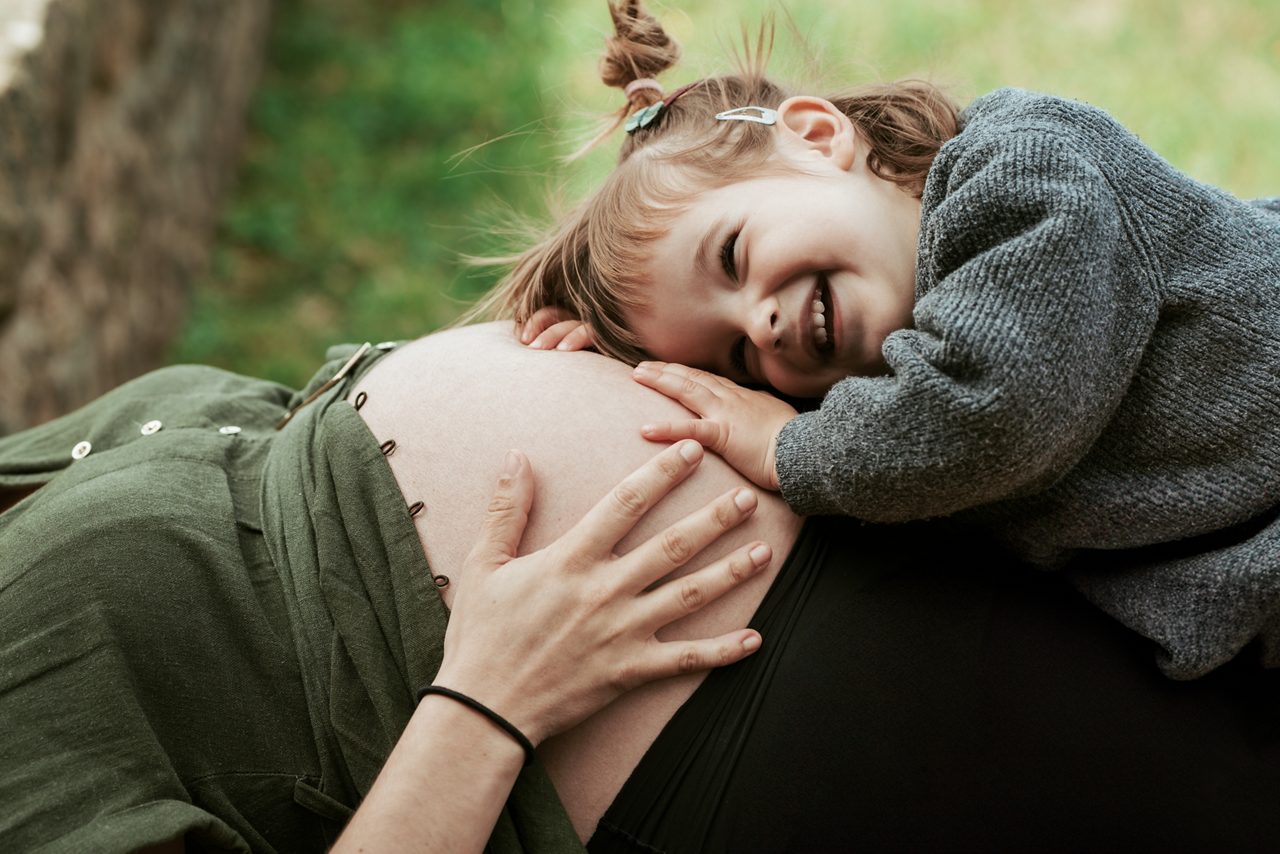 Jong kind speelt liefdevol met haar zwangere moeder