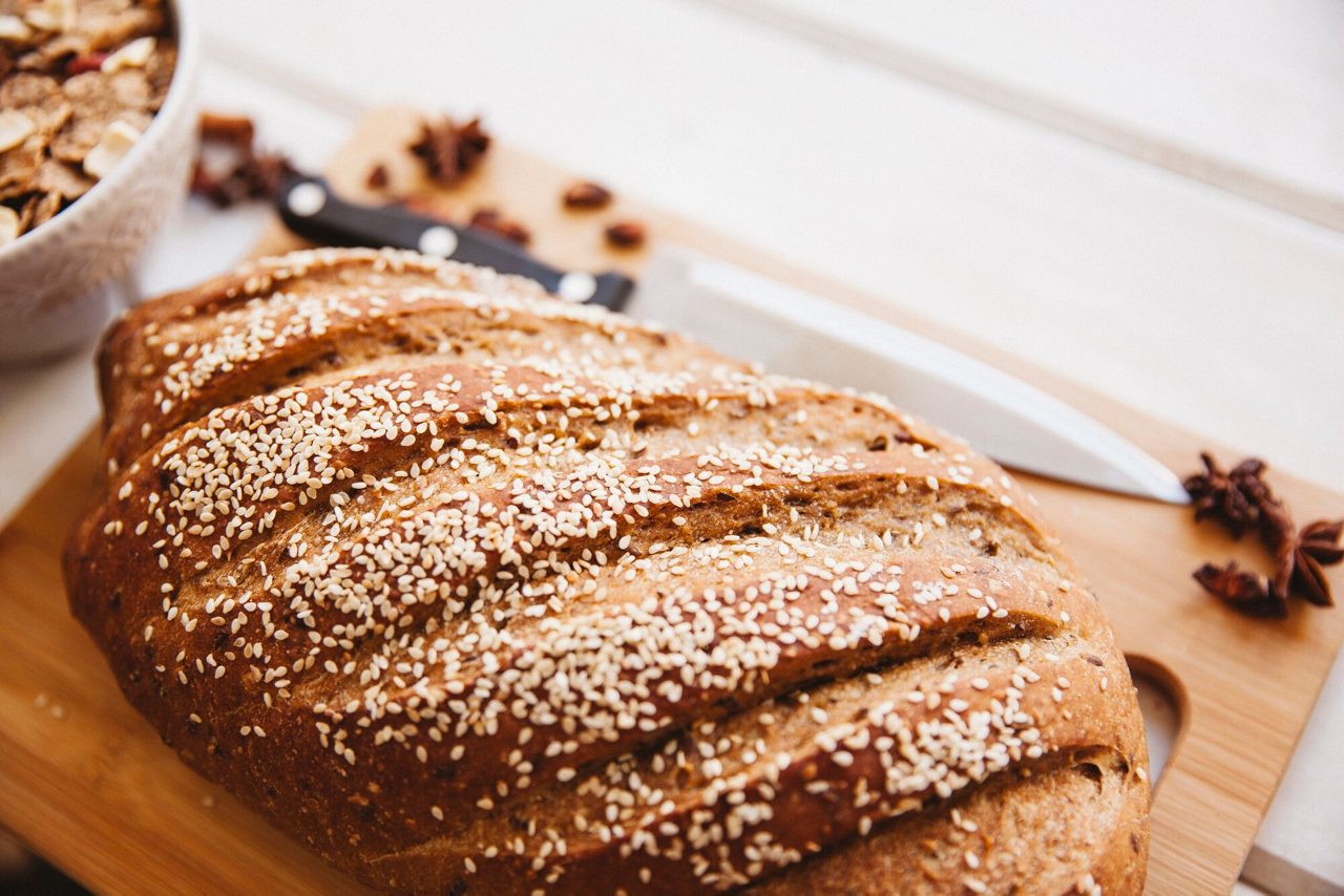 Vers volkoren brood gegarneerd met sesamzaadjes op een houten snijplank.