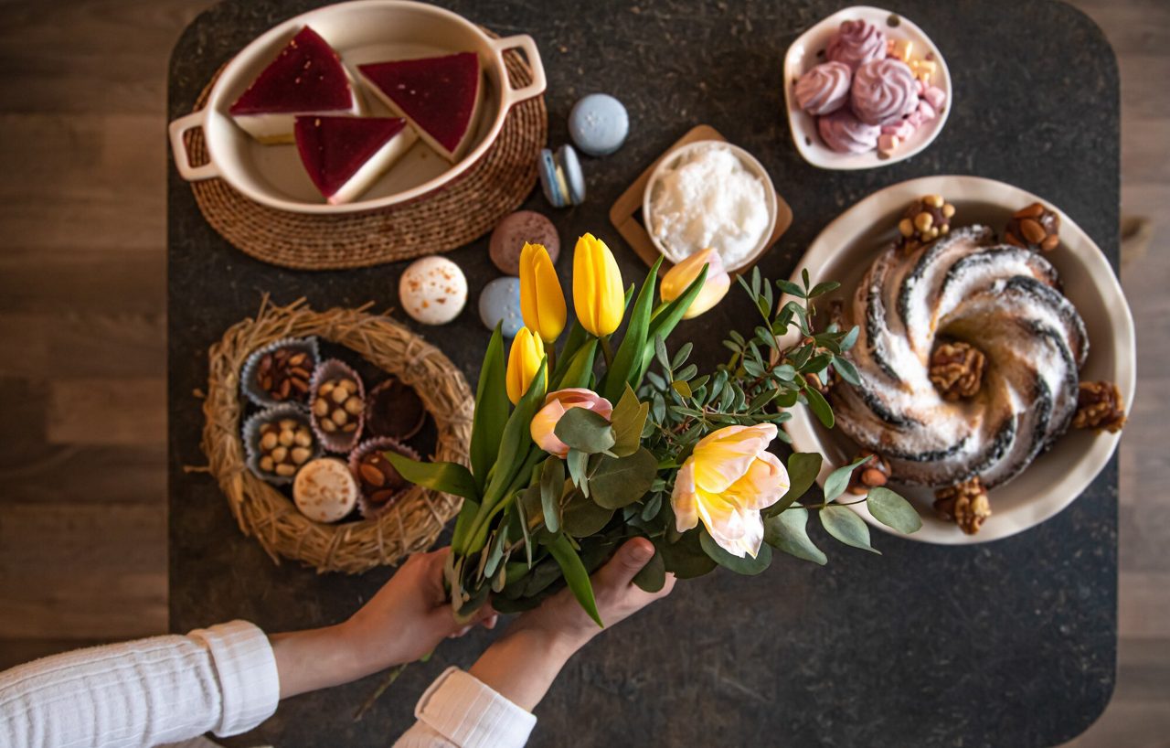 Bovenaanzicht van een desserttafel met diverse gebakjes, snoepjes en een boeket verse tulpen.