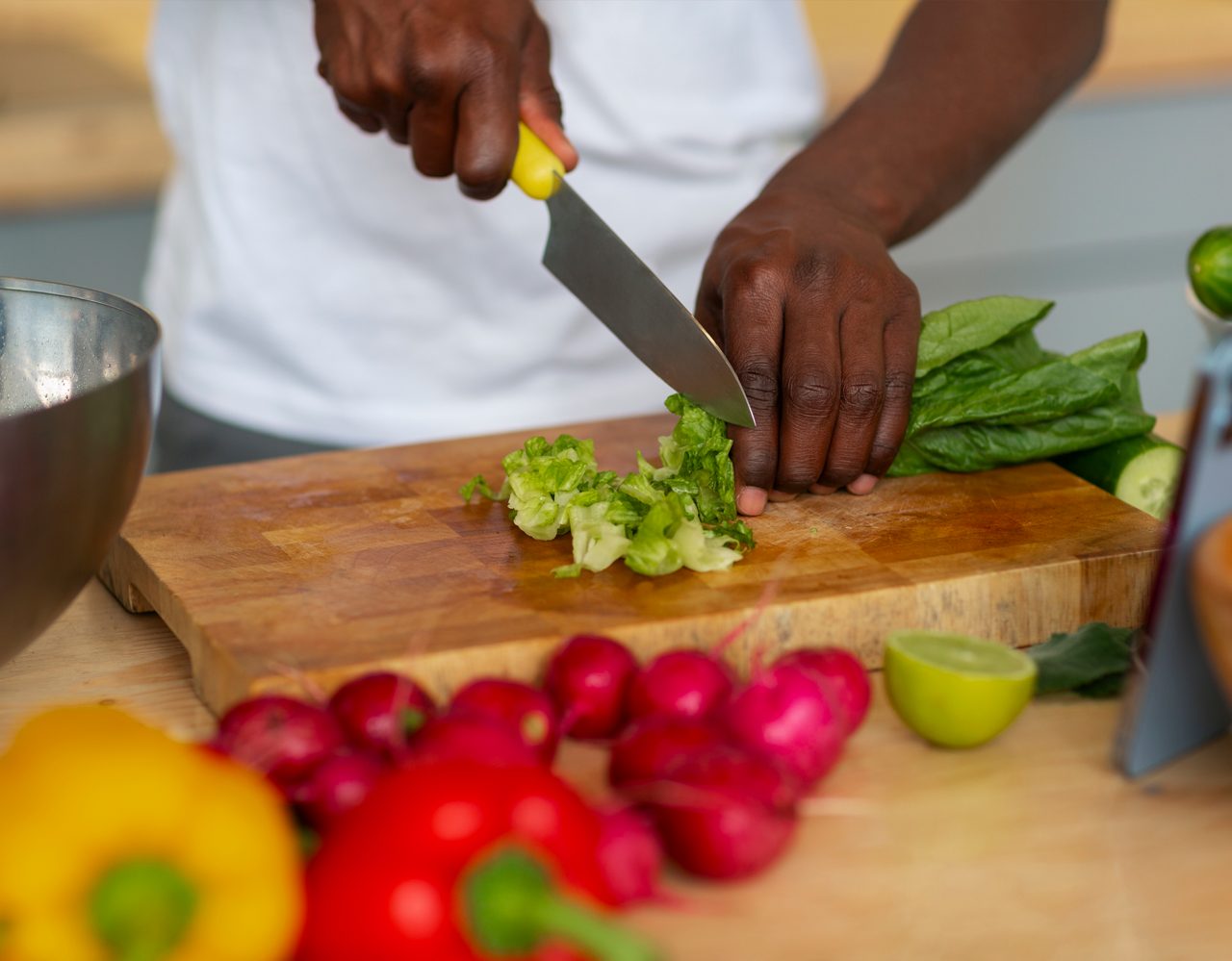 Persoon die komkommer snijdt op een houten snijplank met verse groenten in de buurt.