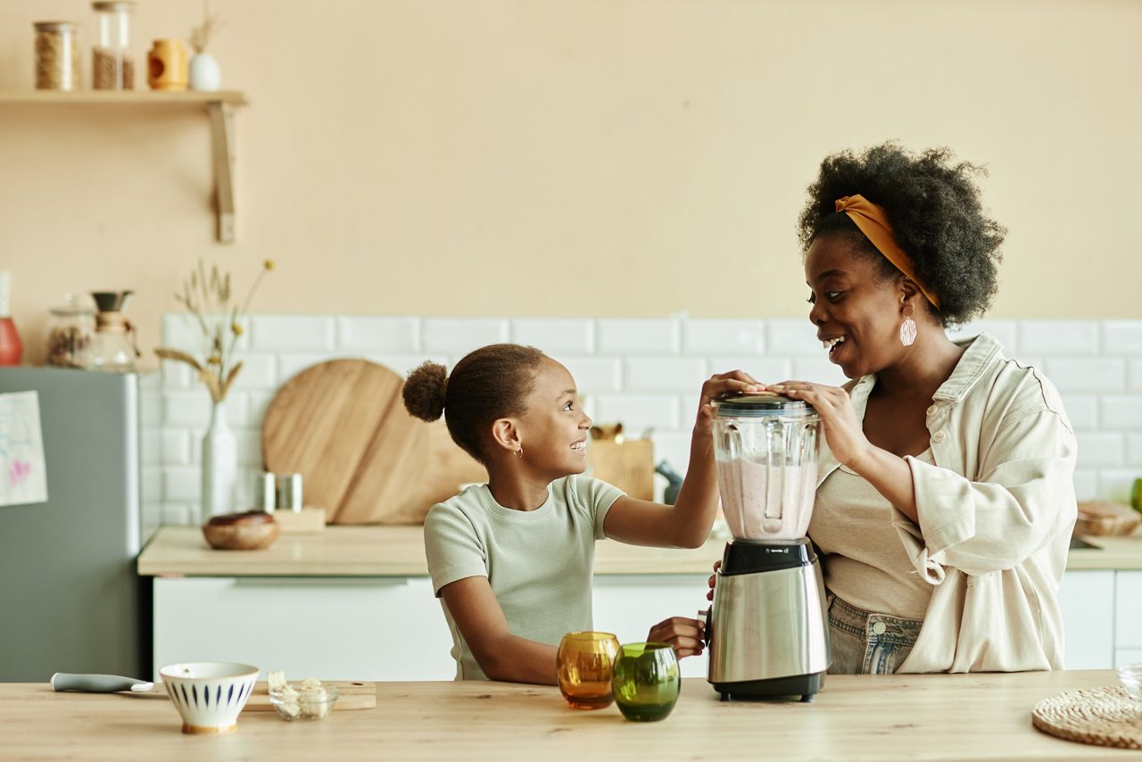 Moeder en dochter glimlachen terwijl ze samen een blender gebruiken in een lichte keuken.