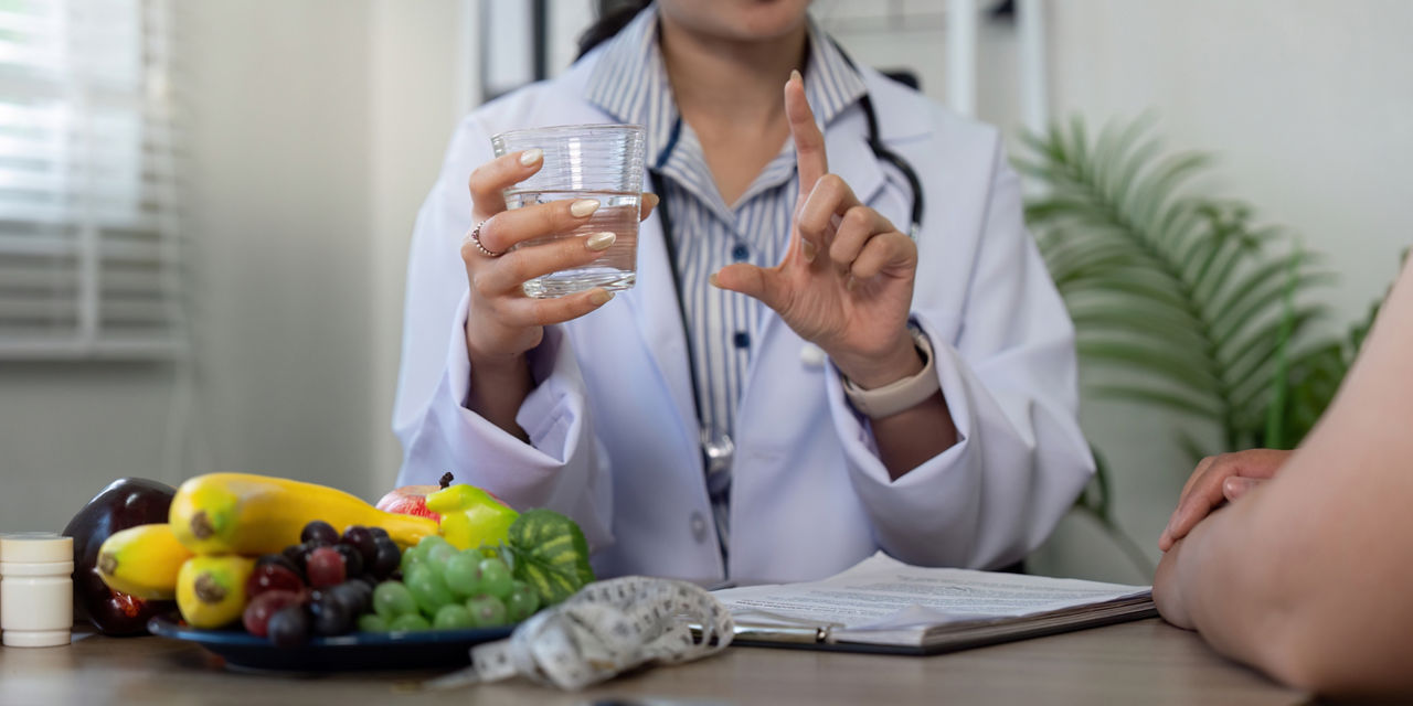 The nutritionist emphasizes hydration while pointing out the variety of fruits available, showcasing a well-rounded diet in a professional setting.