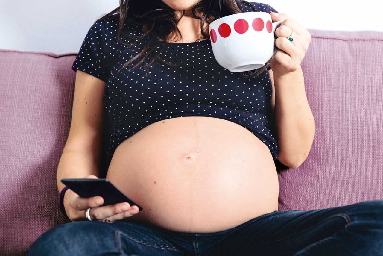 pregnant using cellphone and holding a mug