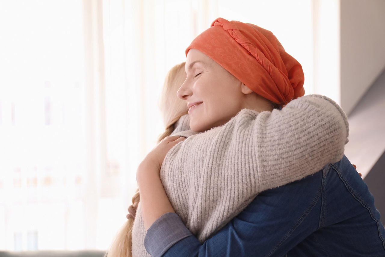 Young woman with cancer hugging her mother indoors