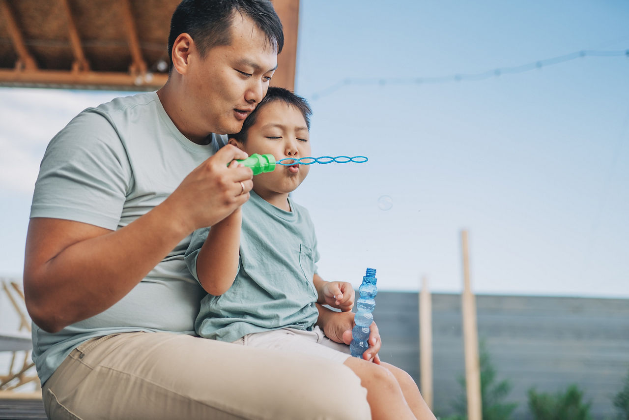 Asian dad and son blowing soap bubbles in the park