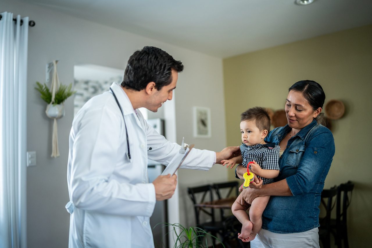 Pediatrist talking and examining baby boy with mother at home