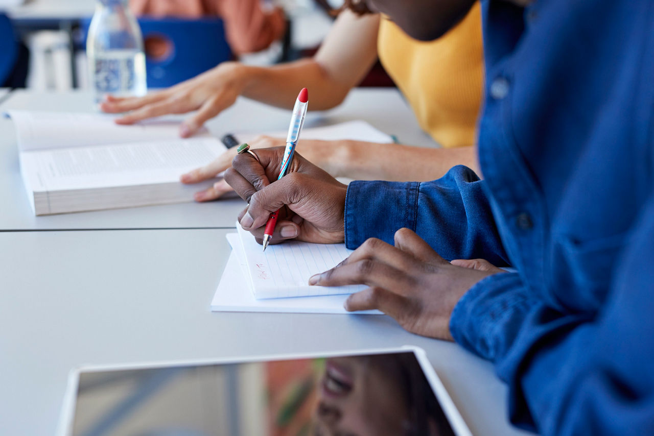 Midsection of man writing in book while sitting with female friend at desk