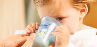 Peuter aan het drinken en zit met moeder op de bank