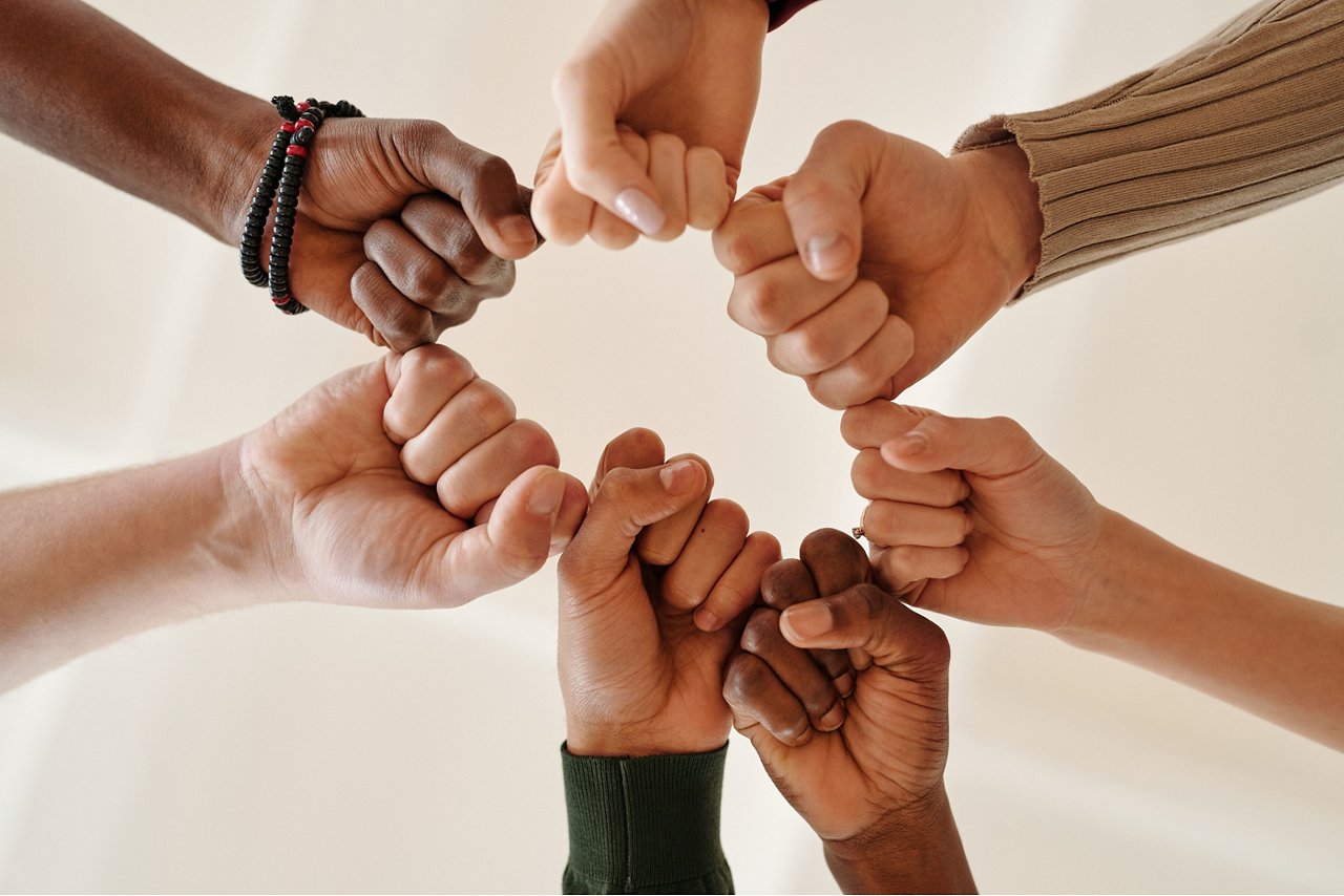 Un groupe diversifié de personnes forme un cercle, les poings réunis, symbolisant la collaboration, la solidarité et l’inclusion.