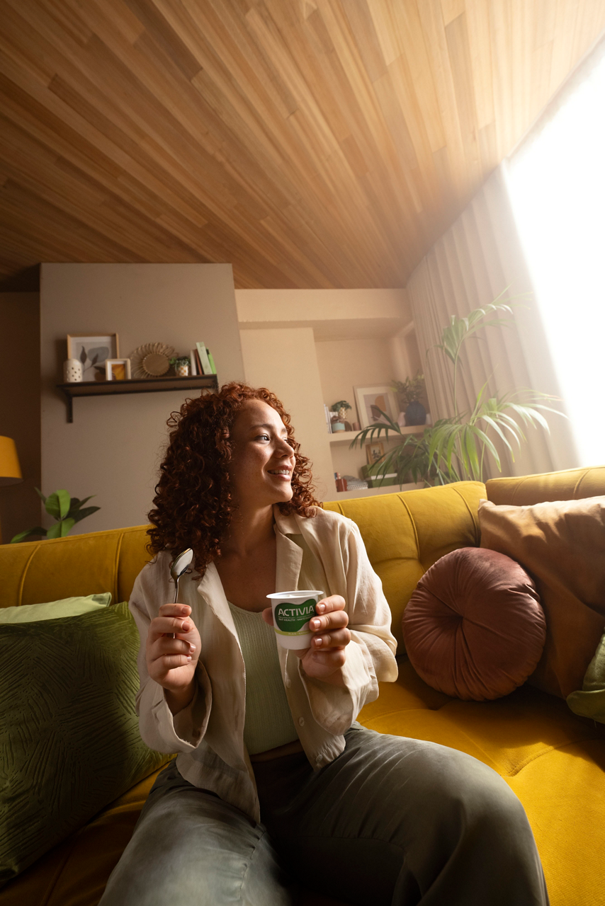 Woman enjoying yogurt on cozy yellow sofa