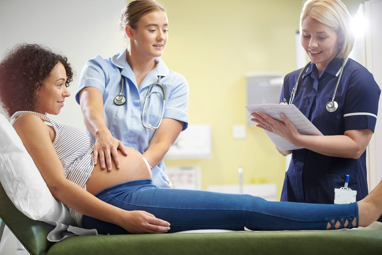 a pregnant lady is examined by young student midwife overseen by a senior nurse