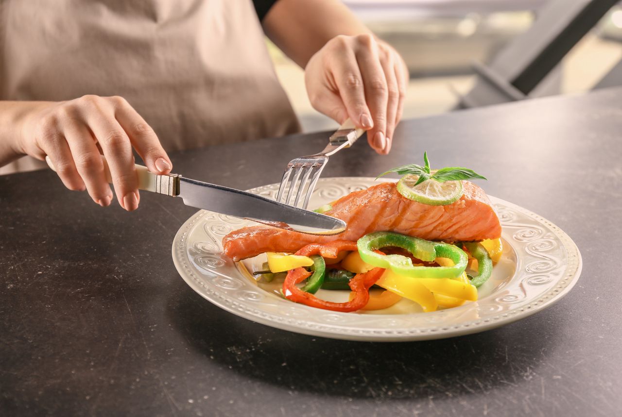 Woman eating tasty salmon with fresh peppers at table