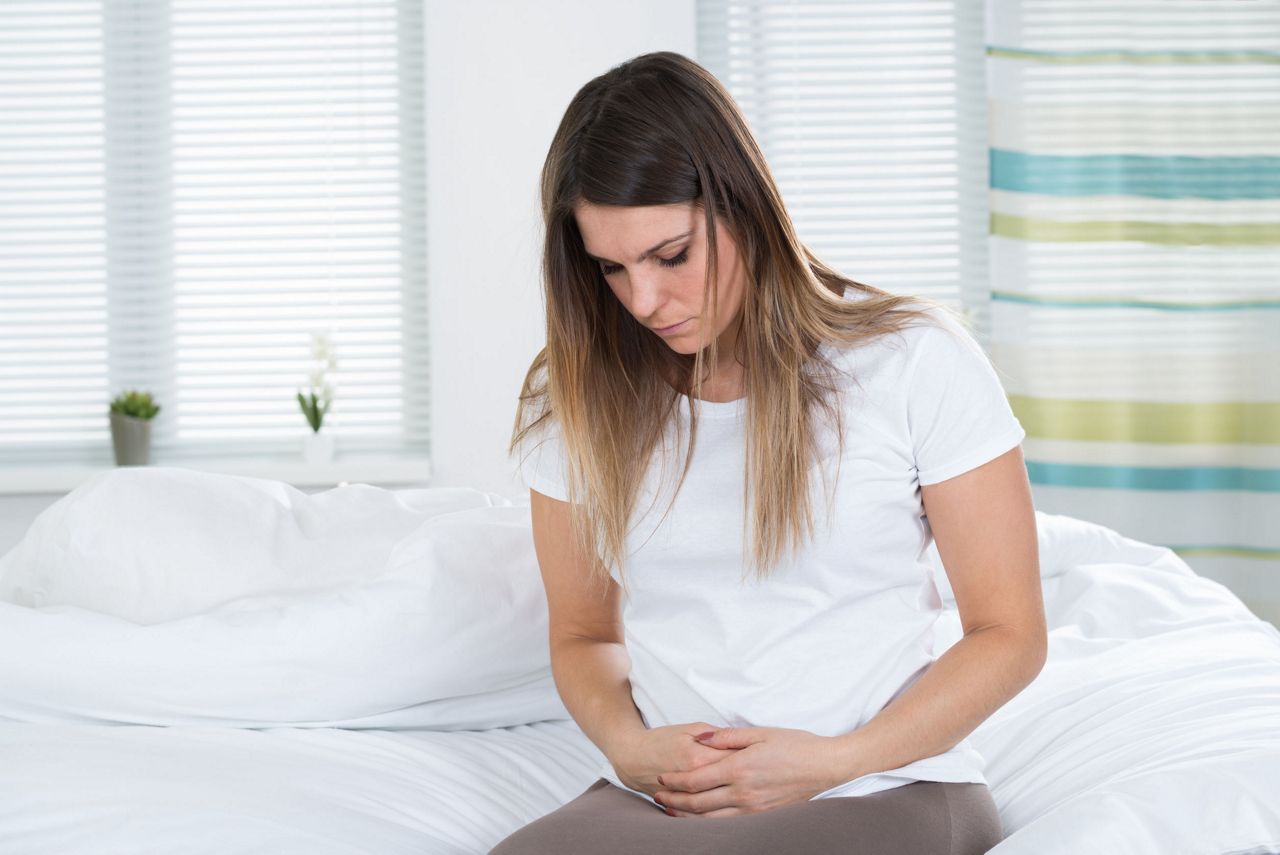 51925362 - unhappy young woman suffering from stomach ache sitting on bed