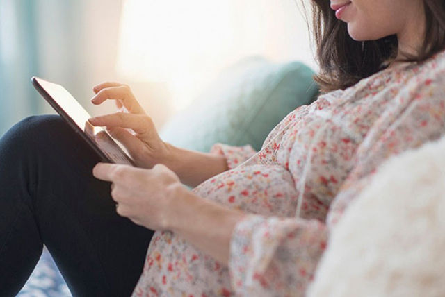 mujer embarazada checando Faceboon con tablet sobre las rodillas