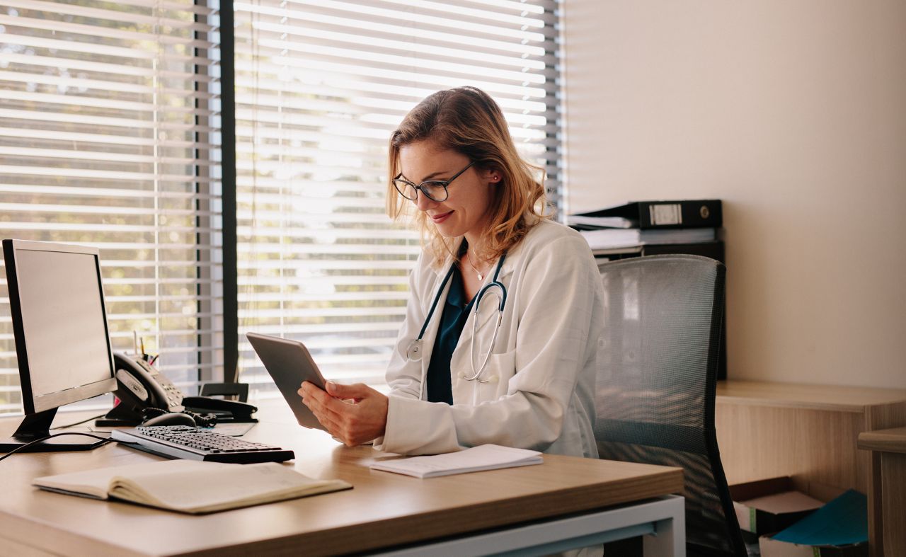 Female doctor using a digital tablet at her desk in the clinic. Female doctor working on her tablet pc in her office.