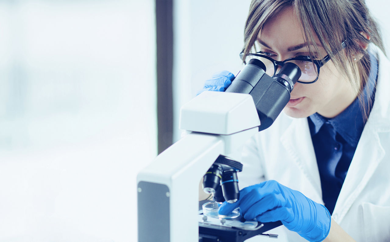 Lady scientist in white lab coat looking through microscope