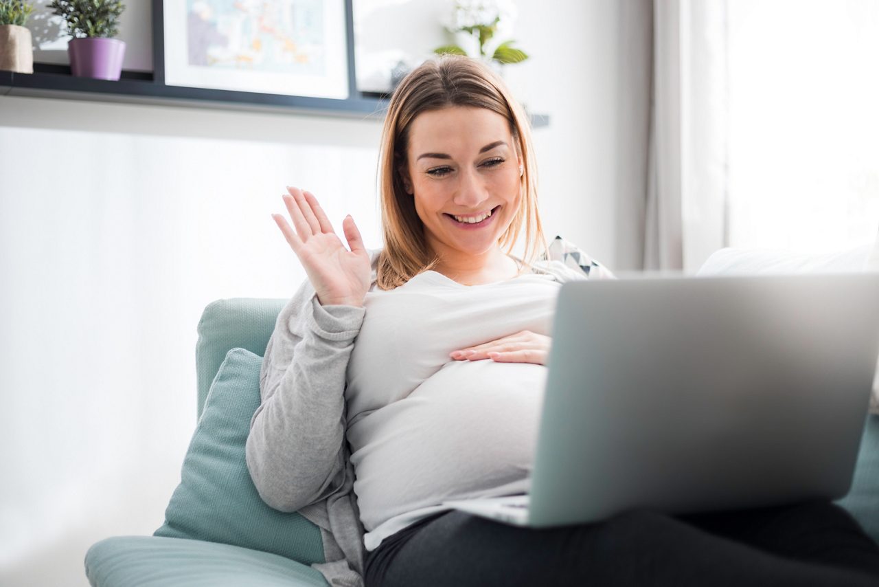 Pregnant woman video chatting with family on laptop waving hand to screen getty images 1209875154