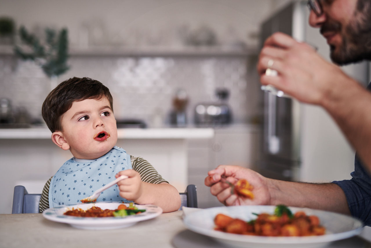 Self feeding baby watching father