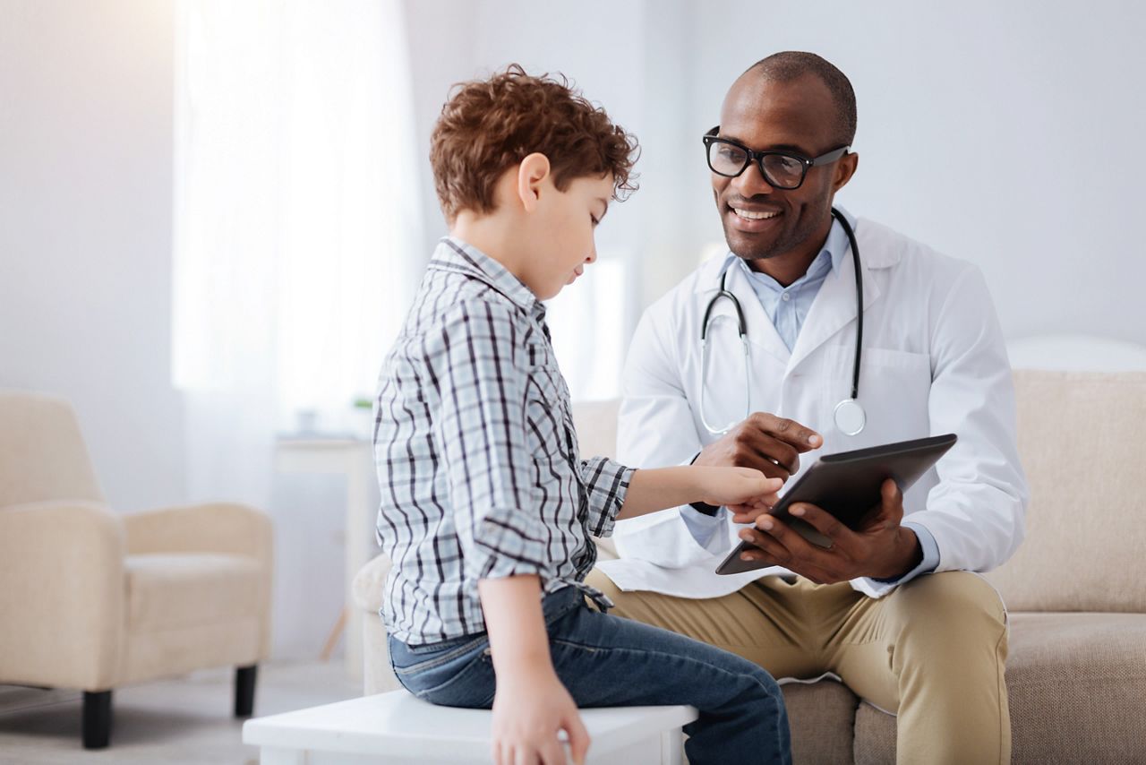 Technology in medicine. Positive pleasant male doctor smiling while showing tablet to boy and sitting; Shutterstock ID 1054597466; purchase_order: DNC Thumbnails; job: Webinars 3 (50/188); client: ; other: 