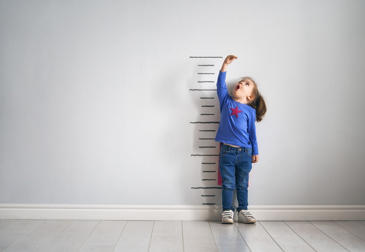 Little child is playing superhero. Kid is measuring the growth on the background of wall. Girl power concept. ; Shutterstock ID 1059882755; purchase_order: DNC Thumbnails; job: Webinars 4 ; client: ; other: 