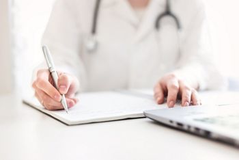 the doctor in a dressing gown with a stethoscope sits at a table and works in a laptop. Medecine, diagnostics and modern technologies