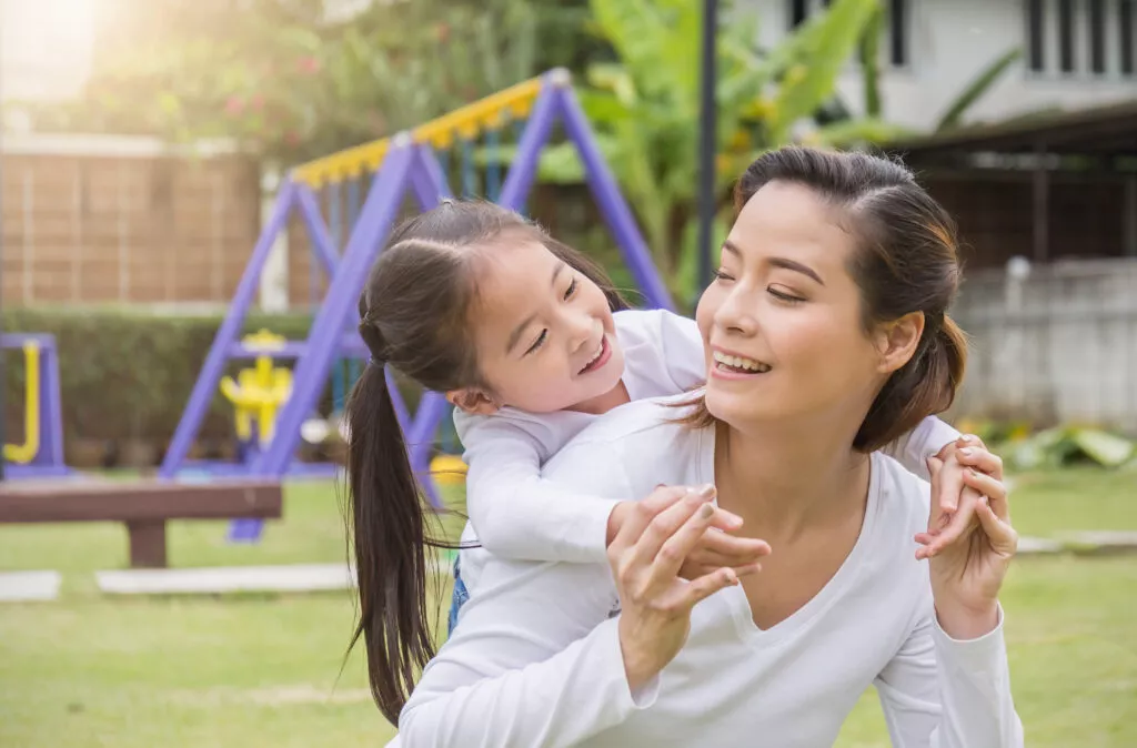 Portrait of happy asian mother and daughter. Asian woman and little toddler girl cuddling and hugging in the playground park. Happy family green spring or summer mother’s day together concept
