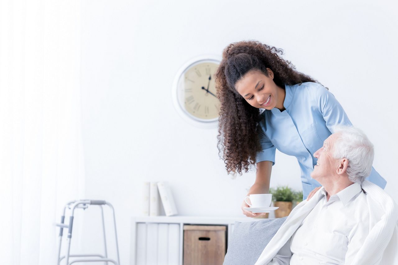 Smiling nurse giving tea to elderly man in the white nursing house; Shutterstock ID 1148329100; purchase_order: DNC Thumbnails; job: Publications; client: ; other: Replace Fishwife