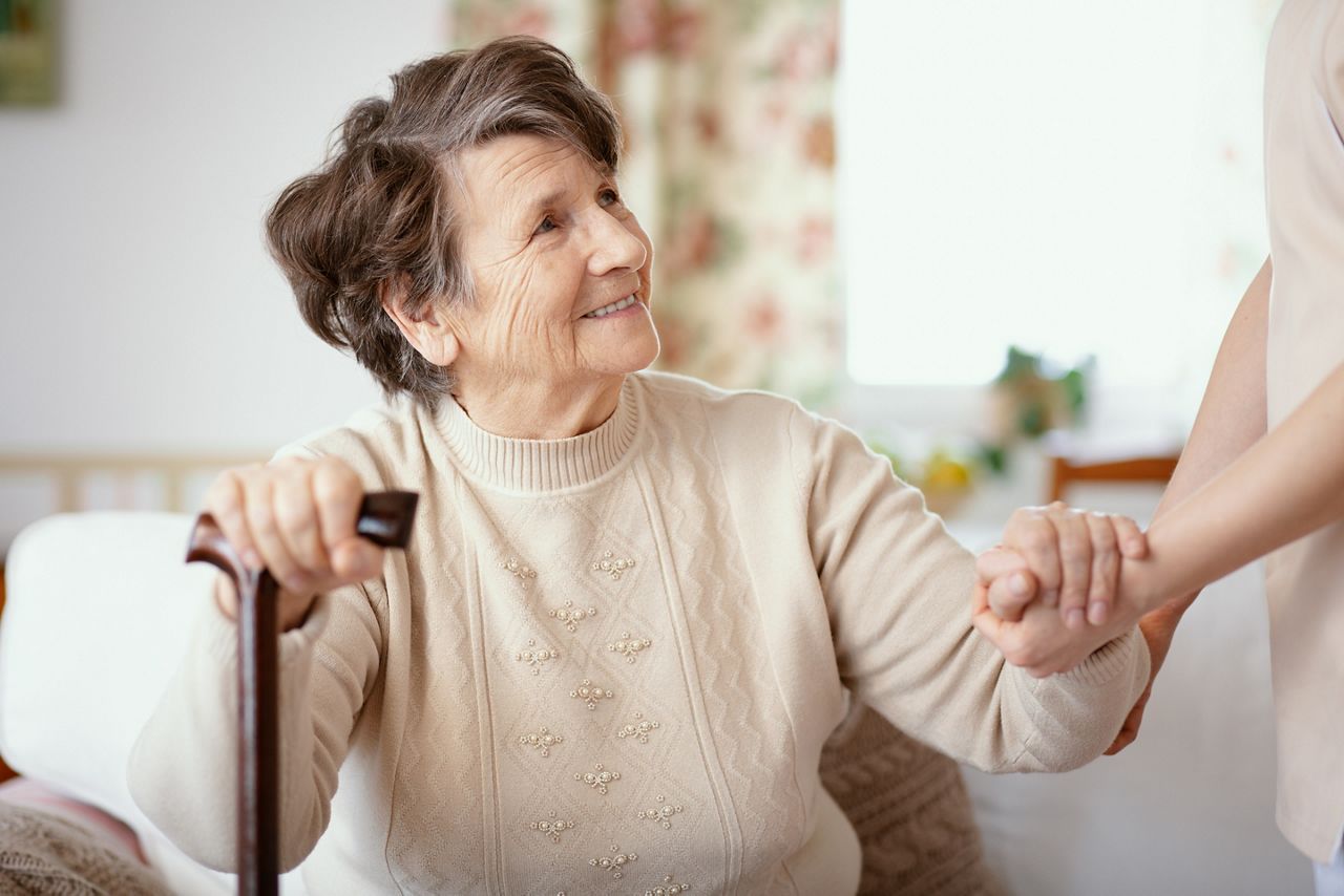 Smiling senior woman with walking stick and helpful caregiver holding her hand; Shutterstock ID 1225176769; purchase_order: DNC Thumbnails; job: Videos; client: ; other: 
