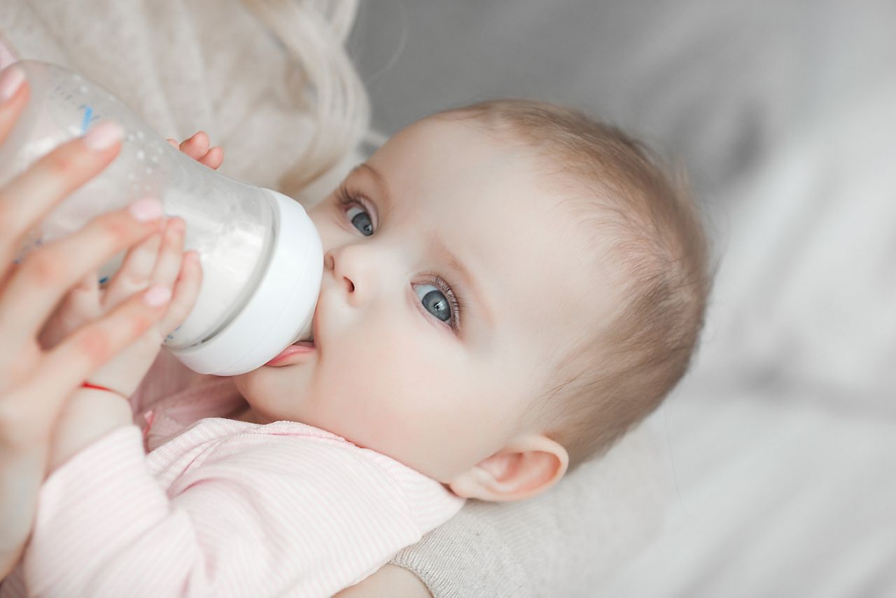 Young mother feeding her little cute baby daughter with bottle of child formula. Woman with her newborn baby at home. Mom taking care of a child. Alternative to breast feeding. ; Shutterstock ID 1300509832; purchase_order: DNC Thumbnails; job: Webinars 3 (50/188); client: ; other: 