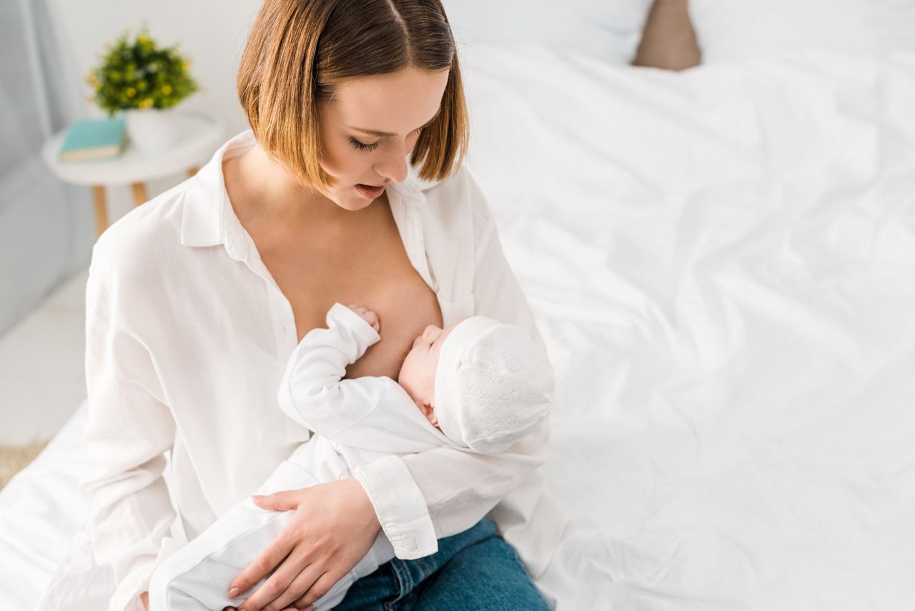 overhead view of young mother in white shirt breastfeeding baby at home; Shutterstock ID 1390770155; purchase_order: DNC Thumbnails; job: Publications; client: ; other: 