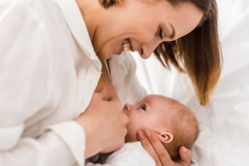 Smiling young mother in white t-shirt breastfeeding baby; Shutterstock ID 1390770179; purchase_order: DNC Thumbnails; job: Booklets; client: ; other: 