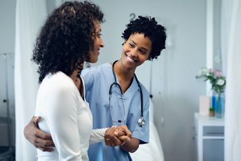 Front view of happy African American female doctor helping female patient to walk in the ward at hospital; Shutterstock ID 1440454943; purchase_order: 25 thumbnail photos ; job: ; client: ; other: 