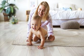 Cute cheerful European infant in diaper having joyful facial expression, laughing while crawling on floor from his smiling mother who is chasing him. Blonde young woman playing with son indoors; Shutterstock ID 1445440928; purchase_order: DNC Thumbnails; job: Infographics; client: ; other: 