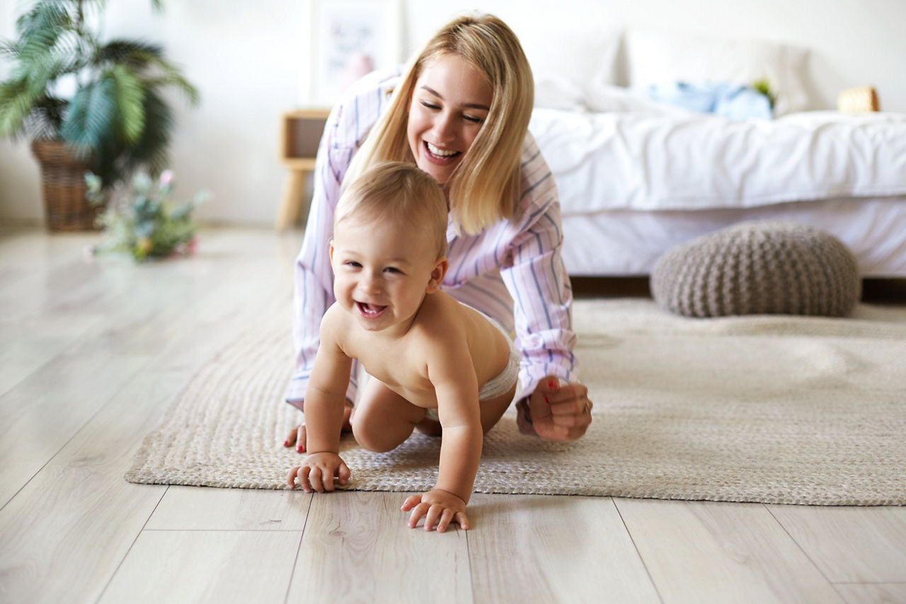 Cute cheerful European infant in diaper having joyful facial expression, laughing while crawling on floor from his smiling mother who is chasing him. Blonde young woman playing with son indoors; Shutterstock ID 1445440928; purchase_order: DNC Thumbnails; job: Infographics; client: ; other: 