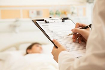 Close up of doctor writing on a medical chart with patient lying in a hospital bed; Shutterstock ID 158328617; purchase_order: DNC Thumbnails; job: Publications; client: ; other: Replace Fishwife
