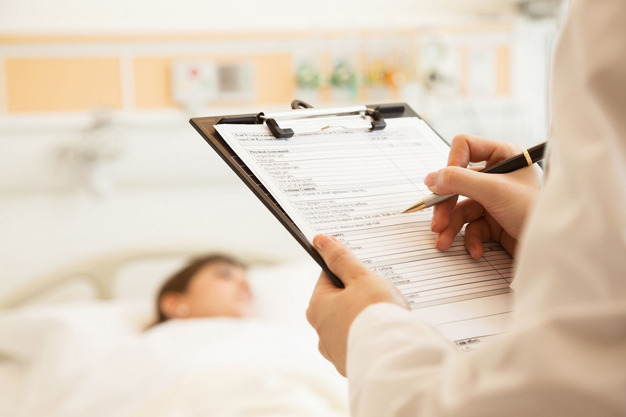Close up of doctor writing on a medical chart with patient lying in a hospital bed; Shutterstock ID 158328617; purchase_order: DNC Thumbnails; job: Publications; client: ; other: Replace Fishwife