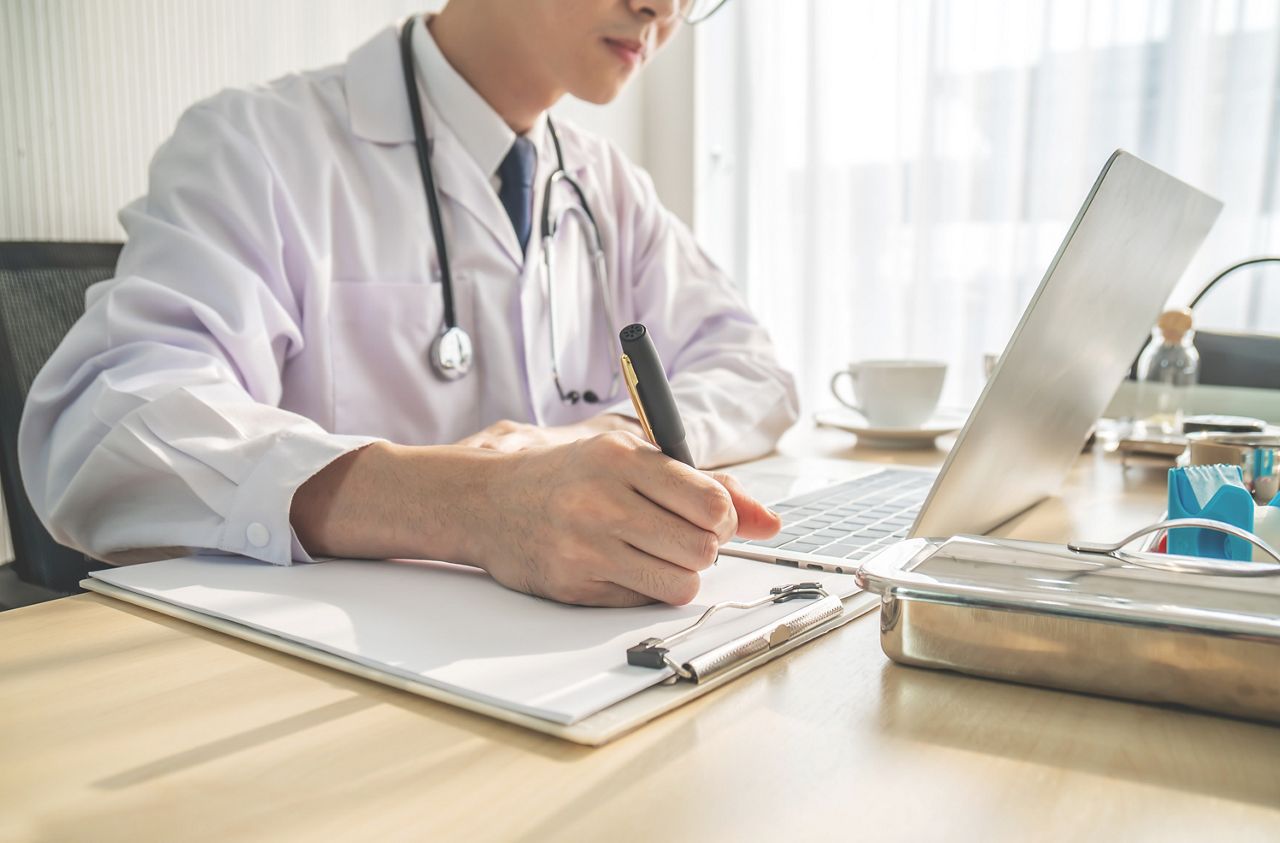 Side view cropped shot of male doctor in white uniform with stethoscope on neck at paperwork with notebook and laptop in the hospital.; Shutterstock ID 1662399052; purchase_order: DNC Thumbnails; job: Publication/Course; client: ; other: Replacements