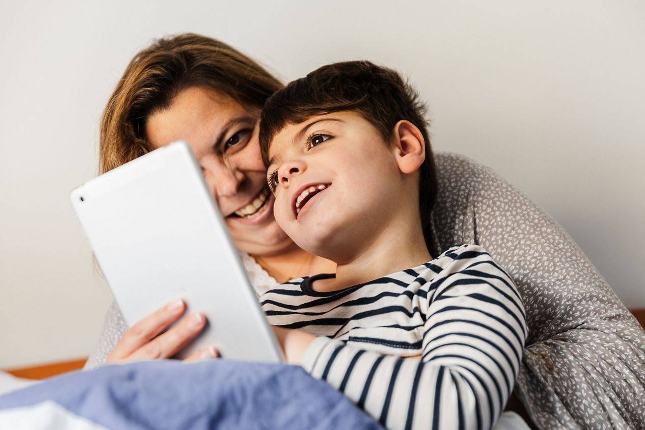 a mother woman and her child with multiple disabilities (handicap, disability) play with the laptop in bed. They are in pajamas, and they are happy and smiling.; Shutterstock ID 1703929912; purchase_order: DNC Thumbnails; job: Webinars 3 (50/188); client: ; other: 