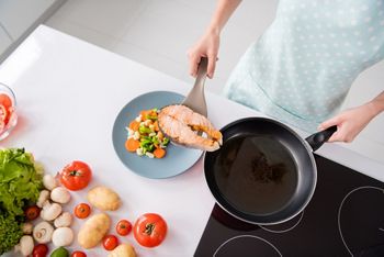 High angle view cropped photo of housewife lady put grilled salmon fillet steak flying pan ready roasted on plate with garnish cooking dinner wear apron t-shirt stand modern kitchen indoors; Shutterstock ID 1718328889; purchase_order: 25 thumbnail photos ; job: ; client: ; other: 