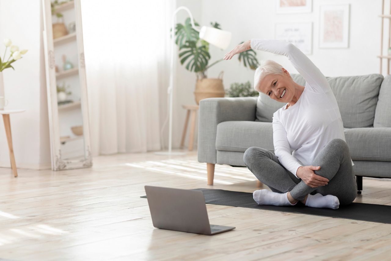 Sport In Mature Age. Happy senior woman doing stretching exercises in front of laptop at home, watching online tutorials, free space; Shutterstock ID 1722150520; purchase_order: DNC Thumbnails; job: Webinars 1 (50/189); client: ; other: 