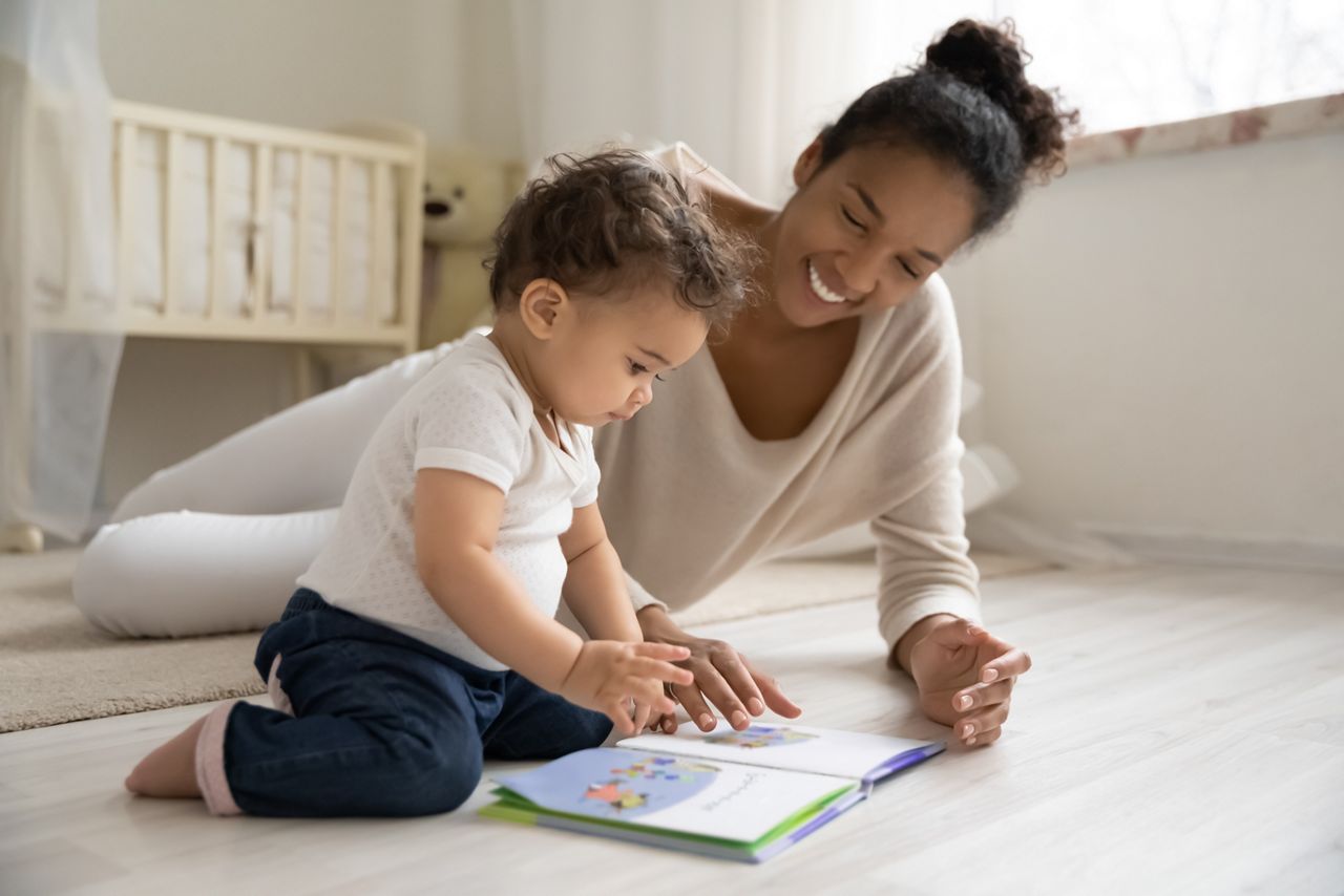 Smiling young african American mother sit on warm floor play with little infant toddler child, happy biracial mom relax have fun read book with small baby girl at home, motherhood, childcare concept; Shutterstock ID 1727021923; purchase_order: DNC Thumbnails; job: Webinars 5 ; client: ; other: Accidentally skipped