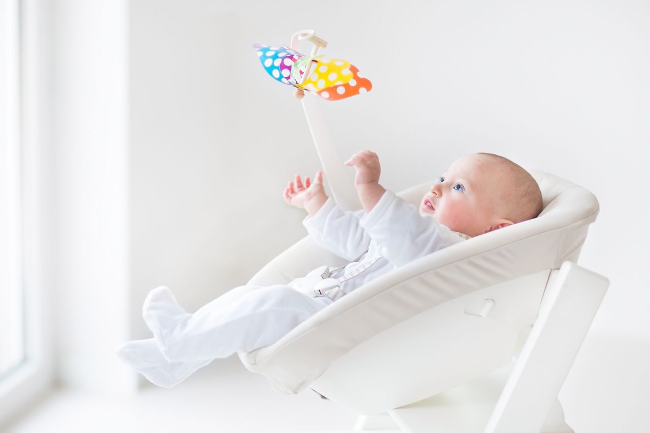Cute newborn baby boy watching a colorful mobile toy sitting in a white high chair next to a window; Shutterstock ID 173543480; purchase_order: DNC Thumbnails; job: Collections; client: ; other: 