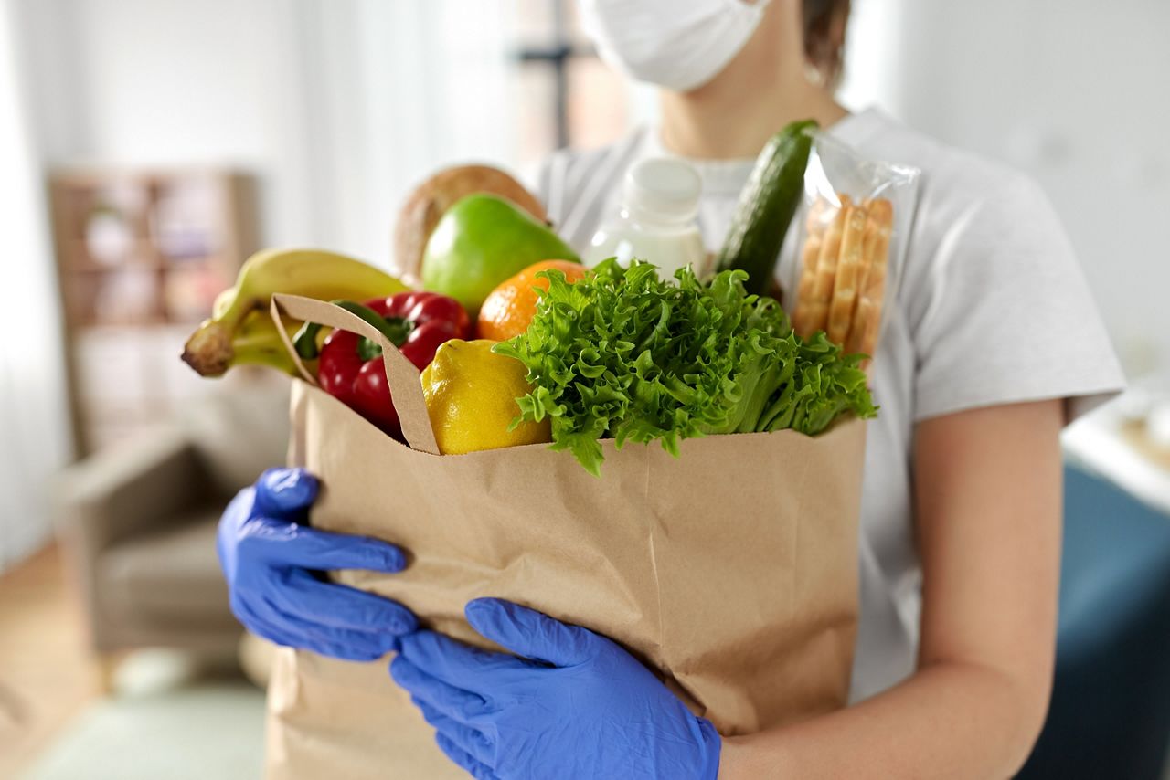 health protection, safety and pandemic concept - close up of woman in protective medical gloves and mask holding food in paper bag at home; Shutterstock ID 1751492597; purchase_order: DNC Thumbnails; job: Webinars 2 (50/188); client: ; other: 