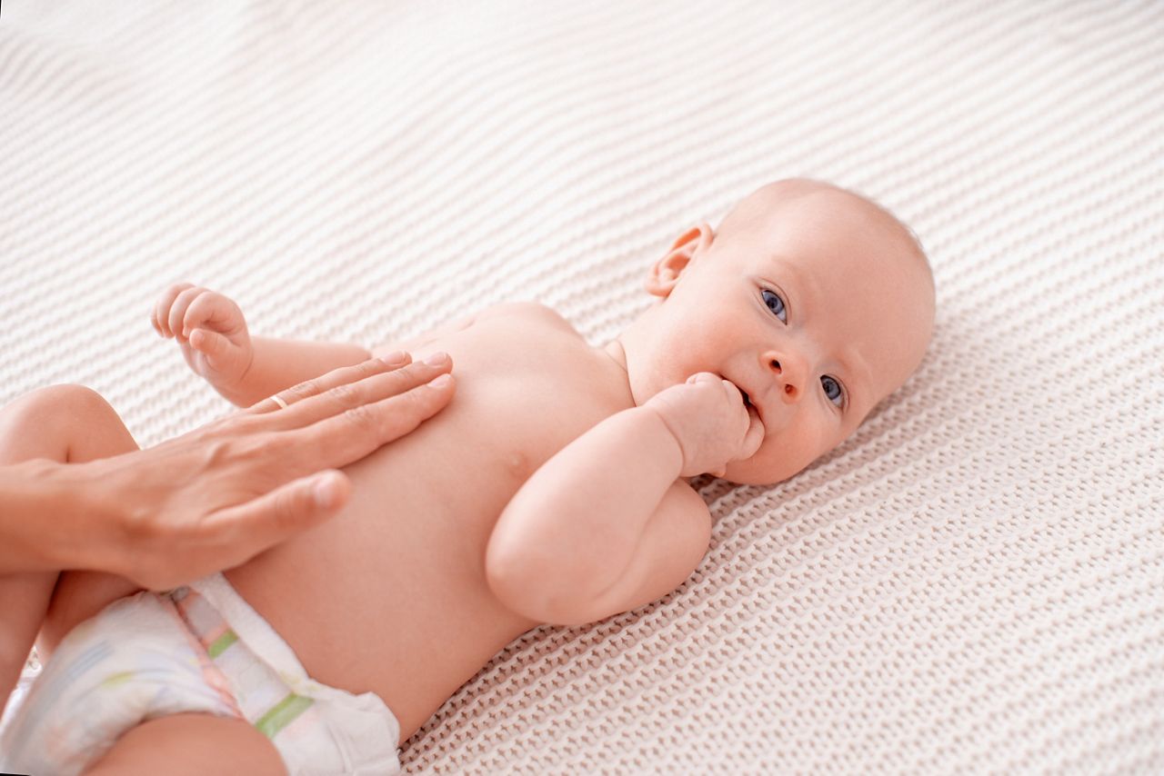 Baby massage. masseur massages baby's tummy during colic. newborn with colic without clothes is lying on his back, mother's hand on his stomach helps her cope with colic. hand in his mouth, teething.; Shutterstock ID 1761764321; purchase_order: DNC Thumbnails; job: Infographics; client: ; other: 